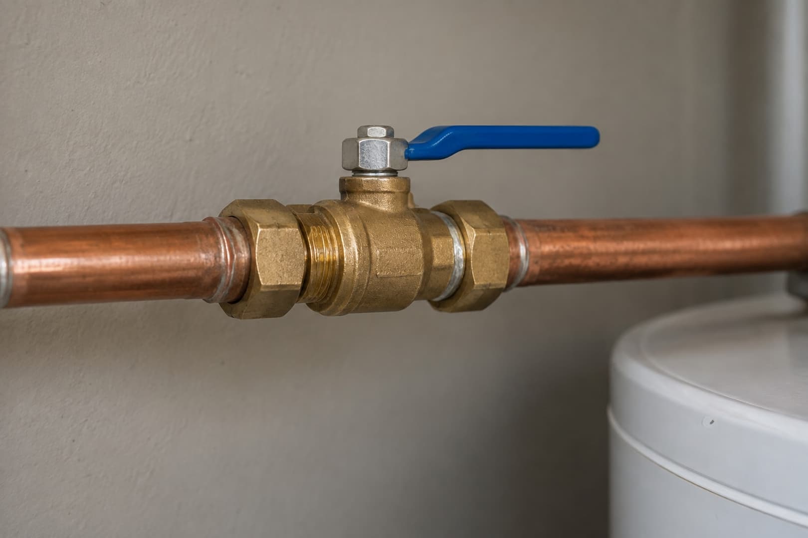 Brass shutoff valve on a copper water pipe beside a storage water heater